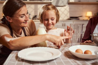 Anne kızının önünde bardağı işaret ediyor.