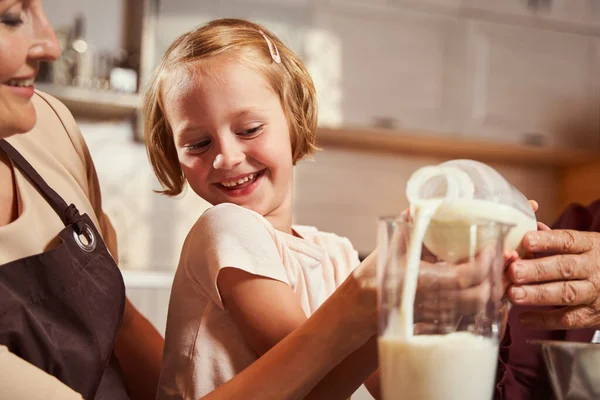 Kind lacht, während sie mit ihrer Familie Glas mit Milch füllt — Stockfoto