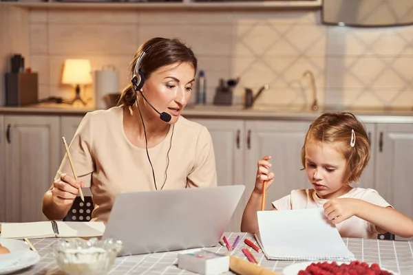 Ragazza disegno in blocco note mentre la madre lavora in remoto sul computer portatile — Foto Stock