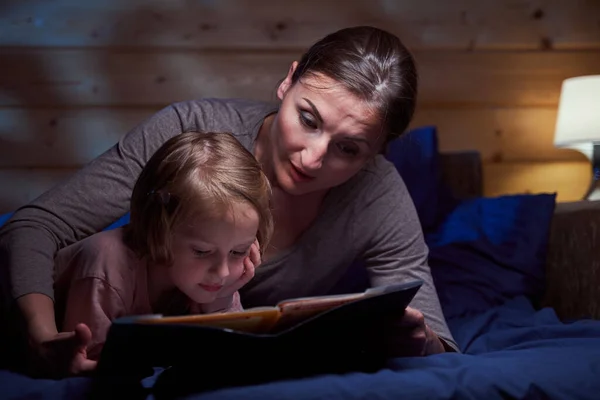 Dítě leží v posteli a čte si pohádky se svou matkou — Stock fotografie