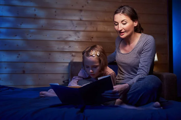 Ragazza che guarda le immagini nel libro di fiabe mentre sua madre legge — Foto Stock