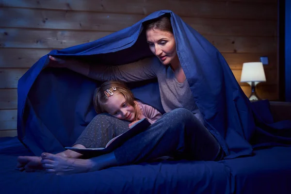 Female and child hiding under blanket while reading — Stock Photo, Image