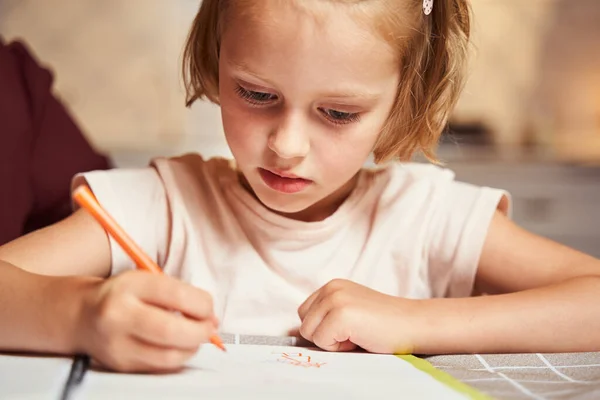 Концентрированный ребенок использует оранжевый маркер для рисования картины — стоковое фото