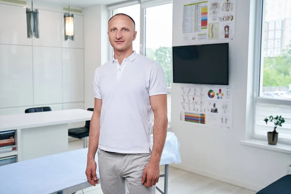 Schöner muskulöser Arzt im weißen Hemd steht in seiner Arztpraxis — Stockfoto