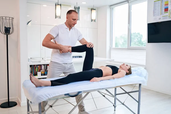 Knappe nette man in wit shirt aan de knie van de patiënt in het wellnesscentrum — Stockfoto