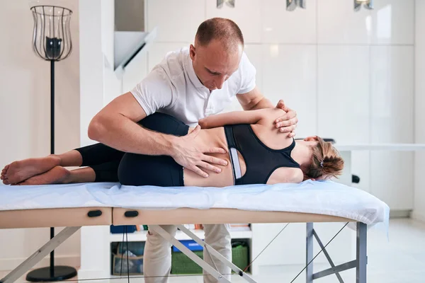 Charmant vrouwtje liggend op massagetafel terwijl dokter osteopaat onderzoek van haar lichaam in medisch centrum — Stockfoto