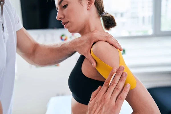 Unrecognized manual therapist taping yellow tape on patient shoulder in wellness center — Stock Photo, Image