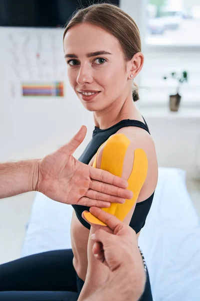 Feliz alegre mujer caucásica recibiendo rehabilitación kinesiología procedimiento en su hombro en el centro de bienestar —  Fotos de Stock