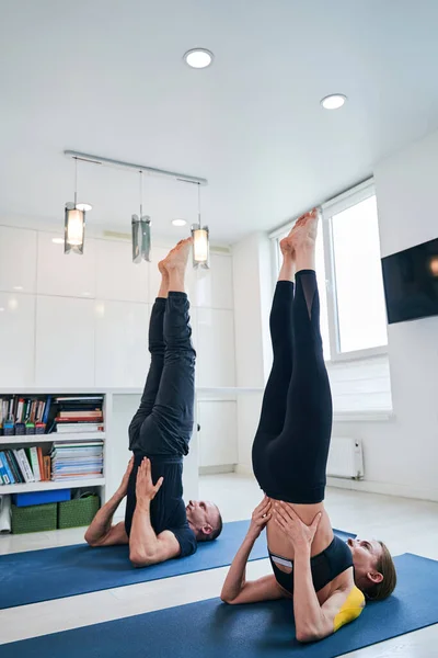 Joven caucásico hombre y mujer haciendo ejercicios de estiramiento en una alfombra de fitness en estudio moderno —  Fotos de Stock