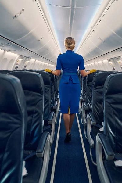 Aeromoça magra com um coque de cabelo em pé no corredor da cabine — Fotografia de Stock