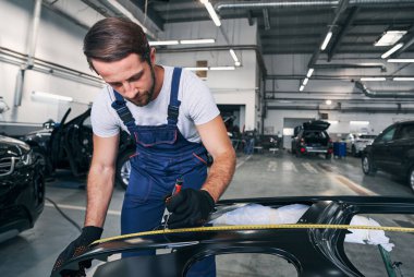 Erkek oto tamircisi araba gövdesinde uzunluk işareti yapıyor