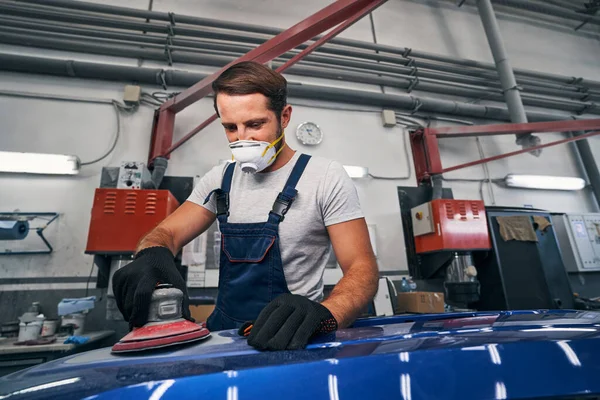 Man in car repair shop sanding automobile with tool — Stock Photo, Image