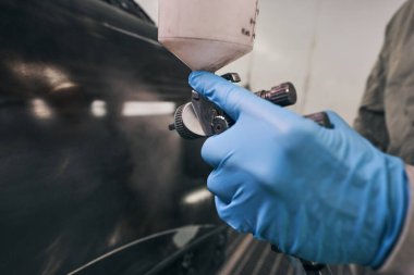 Araba teknisyeni otomobilin yanında sprey tabanca tutuyor.