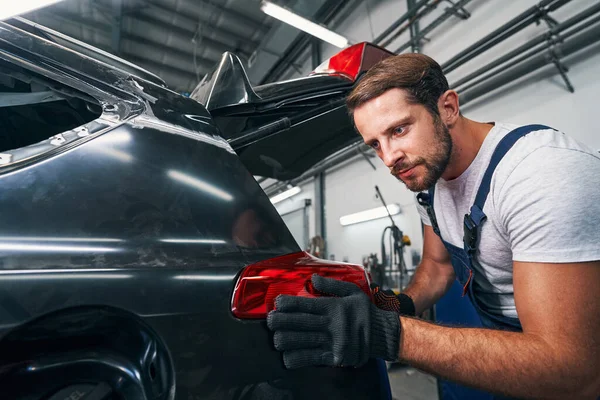 Tachnician is touching rear light of car — Stock Photo, Image