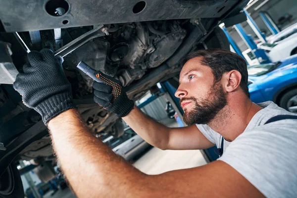 Mecânico está inspecionando carro de baixo com lanterna — Fotografia de Stock