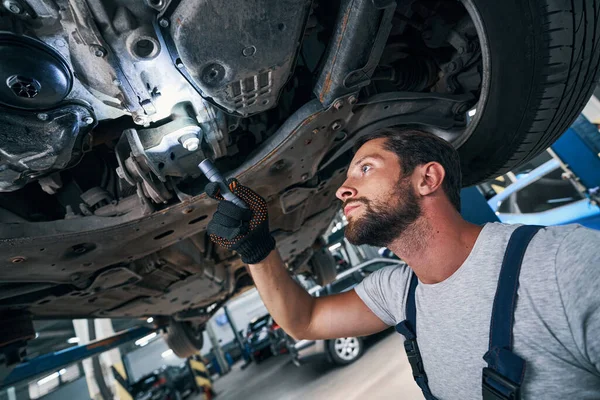 Reparador de automóveis examinando a parte inferior do carro usando lanterna — Fotografia de Stock