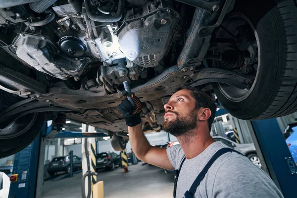 Muž s baterkou pod automobilem studující jeho spodní stranu — Stock fotografie