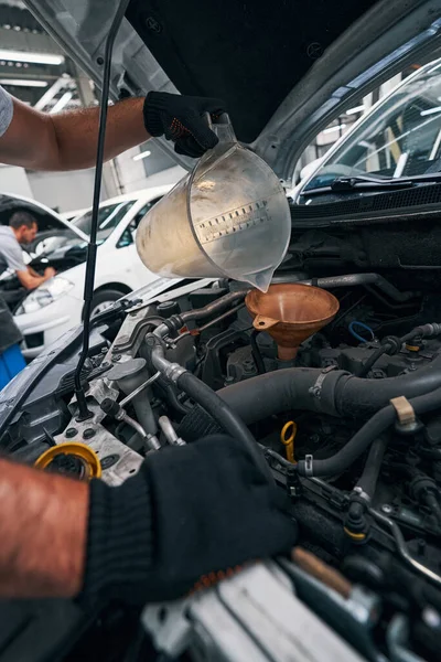 Worker turning over plastic cup while adding oil to engine — Stock Photo, Image