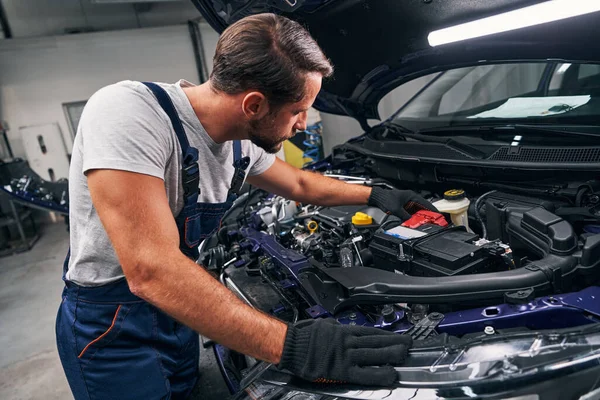 Mecânico profissional ajustando bateria vermelha sob o capô do carro — Fotografia de Stock