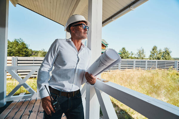 Housebuilder with drawings in arms leaning on porch railings