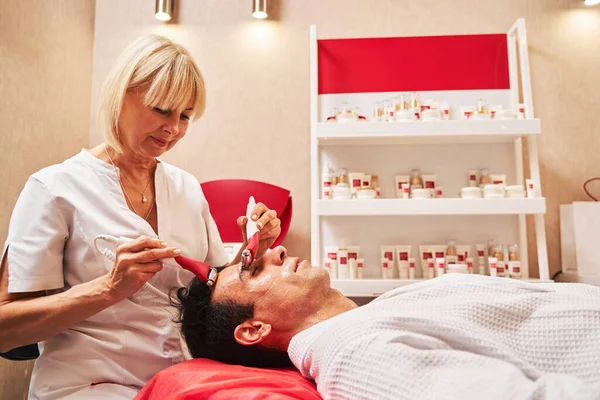 Kvinnlig massagist gör ansiktsbehandling på manligt ansikte med elektricitet — Stockfoto