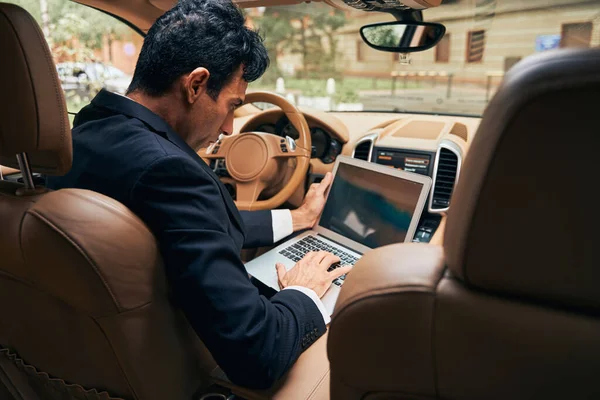 Elegante hombre de negocios que trabaja en el ordenador portátil dentro de un coche — Foto de Stock