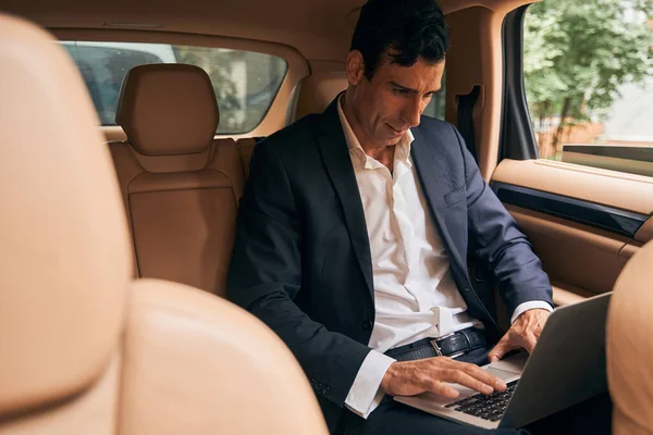 Empresário focado digitando no teclado do laptop do carro — Fotografia de Stock