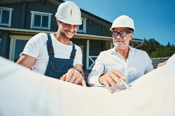 Joyful engineer op zoek naar tekeningen locatie, gewezen door collega — Stockfoto