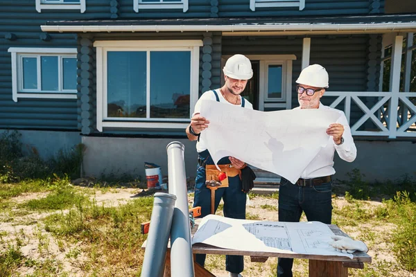 Paret av husbyggare inspektera byggnaden layouter utomhus — Stockfoto