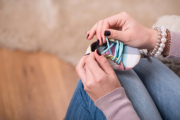 Mujer atractiva joven sosteniendo zapato de bebé, tiro interior —  Fotos de Stock