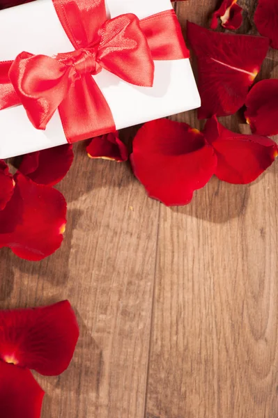 Present box in rose petals on wooden background — Stock Photo, Image