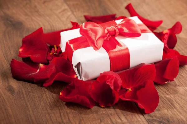 Caja de regalo en pétalos de rosa sobre fondo de madera —  Fotos de Stock