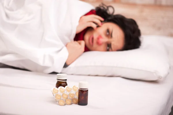 Frustrated woman lying in bed with pills — Stock Photo, Image