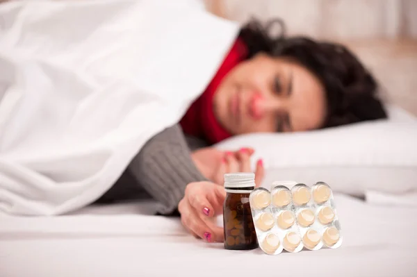 Frustrated woman lying in bed with pills — Stock Photo, Image