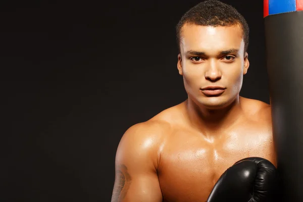 Handsome boxer posing with a punching bag on dark background — Stock Photo, Image