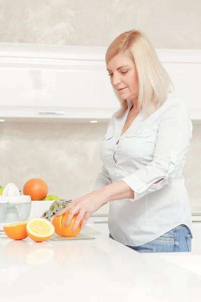 Mulher corta laranjas em uma cozinha — Fotografia de Stock