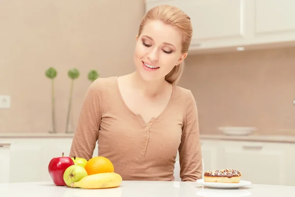 Smiling lady sits between fruit and dessert — Stock Photo, Image