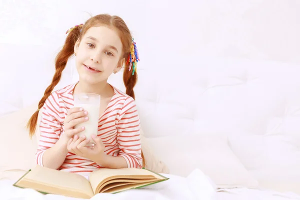 Read-haired girl drinking milk and reading — Stock Photo, Image