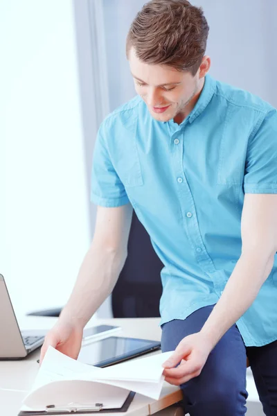 Mann sitzt auf Schreibtisch und blättert in Papieren — Stockfoto