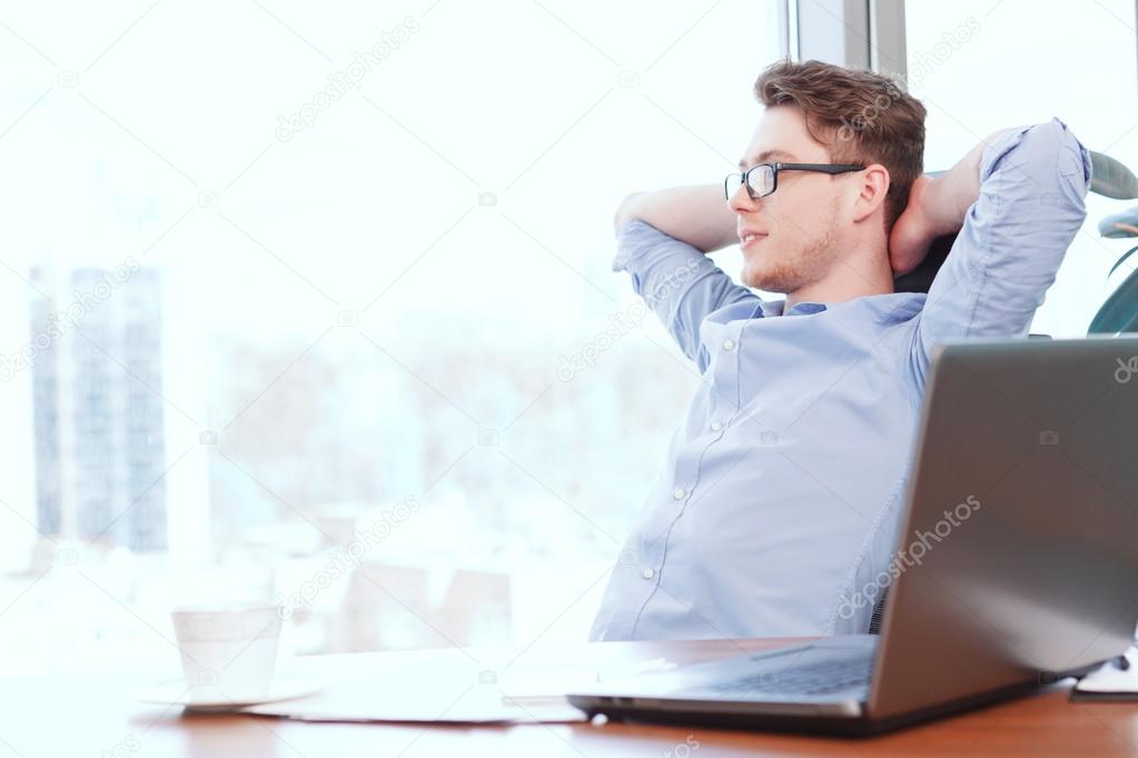 Businessman at desk with hands behind his head