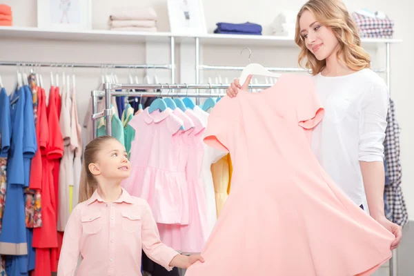 Mãe mostrando um vestido rosa pastel para sua filha pequena — Fotografia de Stock