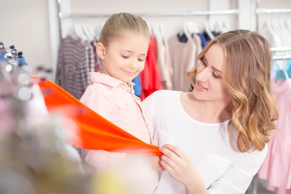 Joven madre con su pequeña hija tocando ropa en una tienda — Foto de Stock