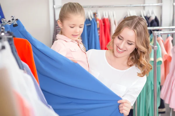 Junge Mutter mit ihrer kleinen Tochter, die in einem Geschäft Kleidung anfasst — Stockfoto