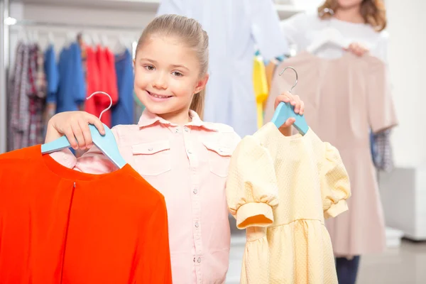 Mother and her daughter holding hangers with colorful dresses — Stock Photo, Image