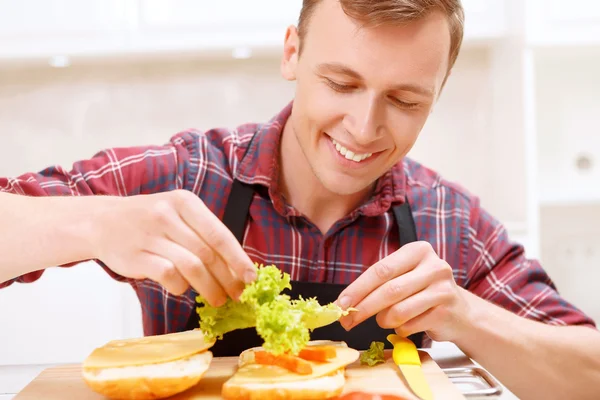 Homem adicionando folhas de alface ao seu sanduíche — Fotografia de Stock