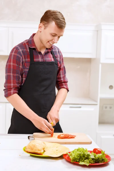 Przystojny mężczyzna krojenie pomidorów w kuchni — Zdjęcie stockowe