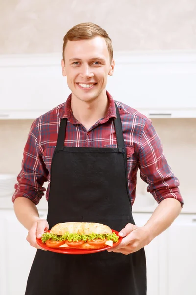 Sorrindo homem segurando prato com sanduíche grande em — Fotografia de Stock