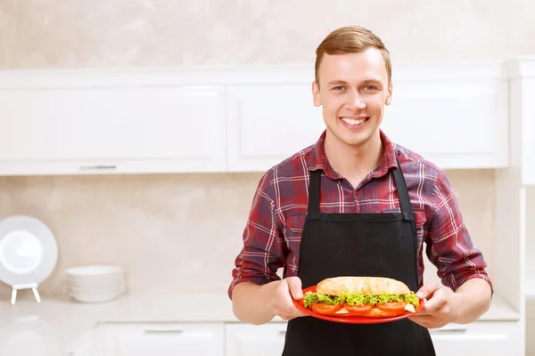 Sorrindo homem segurando prato com sanduíche grande em — Fotografia de Stock