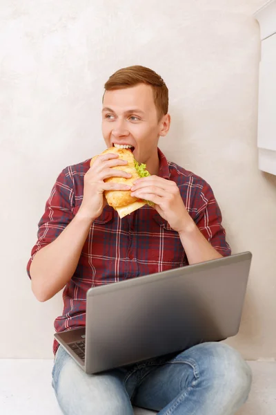 Homem comendo sanduíche e segurando notebook — Fotografia de Stock