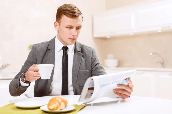 Empresario bebiendo con café cruasán y leyendo periódico —  Fotos de Stock